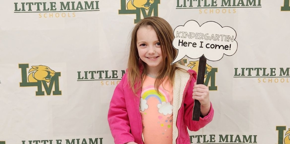 student smiling with sign that says "kindergarten here I come"